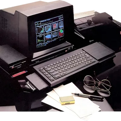 Foto de QL con monitor, ampliación de memoria, disqueteras. Hay unas gafas y unos papeles. En la pantalla se ve el programa Easel mostrando ejemplos de gráficas.